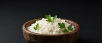 Steamed white rice in rustic wooden bowl garnished with fresh parsley on dark background for healthy meal preparation and cooking concepts.