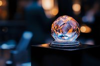 Crystal ball sphere with rainbow reflections on dark surface against blurred bokeh lights background for fortune telling and mystical concepts.