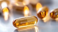 Golden vitamin capsules with omega oil supplements scattered on white surface for health and wellness nutrition concepts.