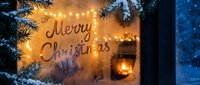 Merry Christmas written on a foggy winter window with warm glowing fireplace lights and snowy fir branches outside on a cold night.