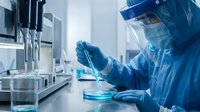 Laboratory scientist in protective suit conducting research with petri dish in sterile medical facility for pharmaceutical development and testing.