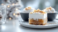 Creamy pumpkin cheesecake bars topped with whipped cream and crushed graham crackers on gray ceramic plate, soft bokeh lights and winter decor background.