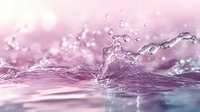 Dynamic water splash with droplets frozen in motion against pink and purple gradient background, creating ethereal and dreamy macro photography effect.