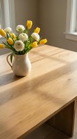 Fresh spring bouquet of yellow tulips and white ranunculus flowers in ceramic pitcher on wooden table near window for home decor and interior design.