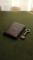Closed brown leather wallet next to silver skeleton key on green fabric surface with soft window light, symbolizing financial security and access to wealth.