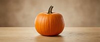 Fresh orange pumpkin on wooden table against warm beige background for autumn harvest decoration and seasonal cooking ingredients.