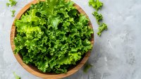 Fresh green curly lettuce leaves in wooden bowl on light gray concrete background, top view. Clean eating and healthy food concept.