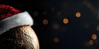 Festive gold Christmas ornament wearing red and white Santa hat against dark background with soft bokeh lights creating magical holiday atmosphere.