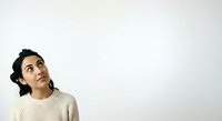 Young South Asian woman with dark hair wearing cream ribbed sweater, looking upward thoughtfully against white background, suitable for lifestyle and contemplation concepts.