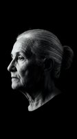 Dramatic black and white profile portrait of elderly Caucasian woman with gray hair in bun against dark background showcasing aging and wisdom.