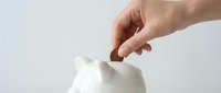 Hand inserting coin into white ceramic piggy bank for savings and financial planning concept on clean background.