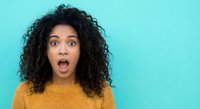 Shocked young African American woman with curly hair expressing surprise and amazement in yellow sweater against turquoise background for advertising.