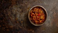 Spicy chili con carne with minced beef, kidney beans and vegetables in metal bowl on rustic dark background. Traditional Mexican comfort food recipe.