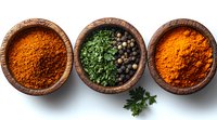Aromatic spices and herbs in rustic wooden bowls arranged in row on white background, featuring vibrant turmeric, dried parsley, black peppercorns and curry powder.