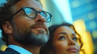 Confident business professionals looking up with aspirational expression against blurred city lights background, representing success and future vision.