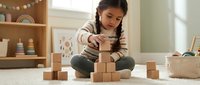 Young Asian girl playing with wooden building blocks on floor in bright modern playroom with educational toys and natural light.