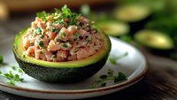 Stuffed avocado half filled with fresh diced vegetables and herbs on white plate. Healthy appetizer or light meal option for nutritious eating and clean diet.
