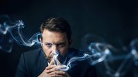 Thoughtful Caucasian businessman in suit smoking, surrounded by swirling smoke against dark background, conveying mystery and contemplation.