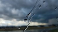 Raindrops on glass surface with blurred stormy sky background creating atmospheric weather scene for seasonal and climate concepts.
