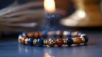 Elegant bracelet with wooden and blue beads featuring ornate metal details, with rising incense smoke creating mystical atmosphere on dark background.