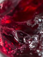 Red wine swirling in glass creates dramatic abstract patterns with bubbles and ripples, captured in extreme macro photography showing rich burgundy tones and liquid motion.