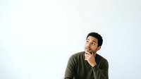 Thoughtful young man with dark hair and olive skin wearing olive green shirt, hand on chin, looking upward in contemplative pose against white background.