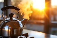 Steaming kettle on stove during golden sunrise, steam rising from spout against warm morning light creating cozy atmospheric kitchen scene.