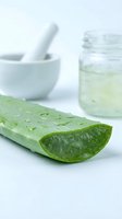 Fresh aloe vera leaf with water droplets, mortar and pestle, and gel extract in glass jar for skincare, cosmetics, and natural remedy applications.