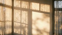 Warm sunlight streaming through vintage window creating geometric shadow patterns on textured wall surface during golden hour morning light.