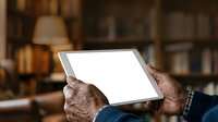 Close-up of senior male hands holding blank tablet device with white screen in home library setting, suitable for technology, education, and digital content mockups.