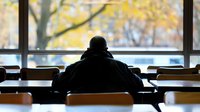 Silhouette of student studying alone in empty classroom with autumn view through windows, creating mood of solitude and focus in academic setting.