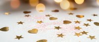 Golden confetti stars and circles scattered on white surface with warm bokeh lights creating festive celebration atmosphere for party decorations.