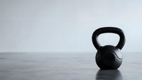 Black kettlebell on wooden floor against white wall in minimalist gym setting for fitness and strength training workouts.