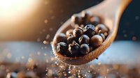 Aromatic black peppercorns in wooden spoon with soft bokeh background and water drops, macro food photography for culinary and cooking concepts.