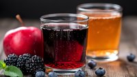 Fresh berry juice drinks with red and amber colors served in glasses alongside fresh blackberries, blueberries and red apple on wooden surface.