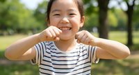 Happy Asian girl child showing strong muscles flexing biceps outdoors in park wearing striped shirt smiling confidently demonstrating strength and power.
