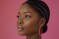 Young African American woman with braided hairstyle wearing vibrant makeup and hoop earrings against pink background, showcasing modern beauty and fashion trends.