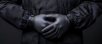 Close-up view of hands in black latex gloves crossed behind back against dark clothing, creating mysterious and professional atmosphere for security concepts.