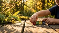 Young child playing with colorful alphabet blocks spelling GROW on wooden surface outdoors in golden sunlight with natural fern background for learning.