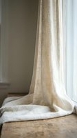 Natural linen curtains hanging by window with soft sunlight creating warm atmosphere in minimalist interior space for home decor and textile design.