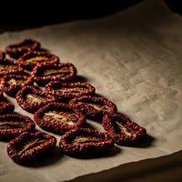 Dried tomato slices arranged on parchment paper with rich red color and wrinkled texture for culinary and food preservation concepts.