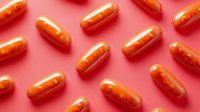 Orange medical capsules scattered on pink background in minimal pattern layout, pharmaceutical and healthcare concept for drug prescription and medication treatment.