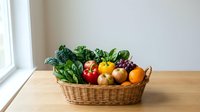 Fresh organic vegetables and fruits in wicker basket on wooden table by window. Healthy eating, farm produce, kitchen counter display for cooking preparation.
