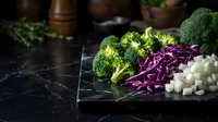 Fresh broccoli, purple cabbage and cauliflower on dark marble surface for healthy cooking and meal preparation.