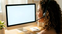 Mixed race woman with curly hair wearing headset working at computer in modern office environment for customer service and remote work applications.