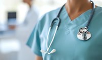 Medical professional in turquoise scrubs with stethoscope standing in hospital corridor, selective focus on medical equipment and uniform details.