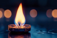 Burning candle flame reflected in water with soft bokeh lights in dark blue background creates peaceful atmospheric mood for meditation and spa.
