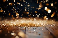 Golden glitter scattered on dark wooden surface with magical bokeh lights and sparkles floating in air creating festive atmosphere for holiday designs.