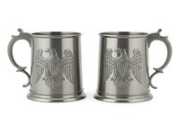 Pair of vintage pewter beer steins with embossed eagle motifs and curved handles, isolated on white background for design and product use.
