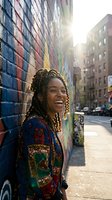 Happy young African American woman with braids laughing against colorful street art mural in urban city setting with bright sunlight and lens flare.